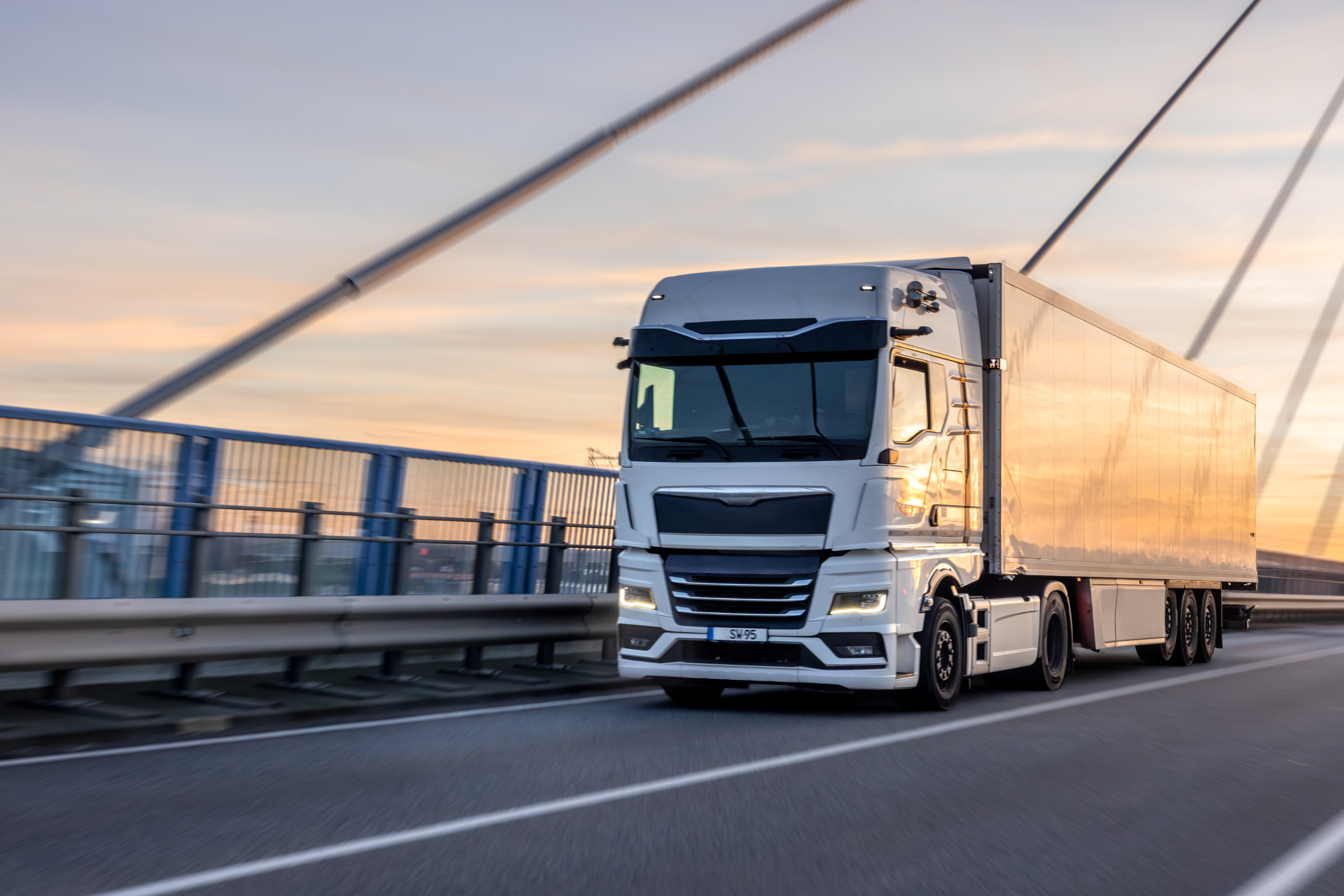 White truck crossing bridge at sunset. Urban logistics in motion.